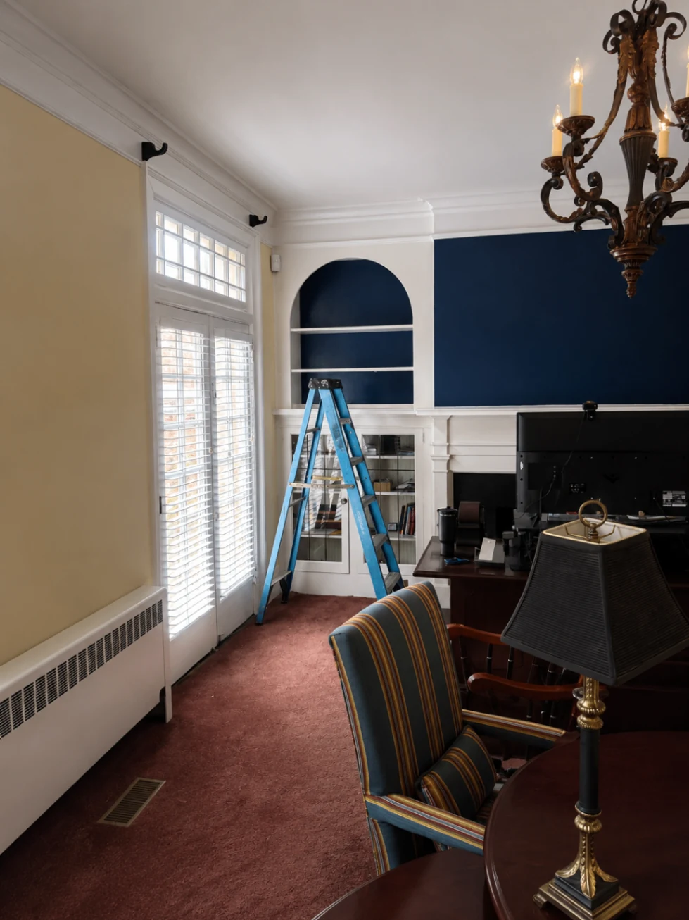 Painting and finishing in progress on navy built-in shelving and feature wall with ladder visible